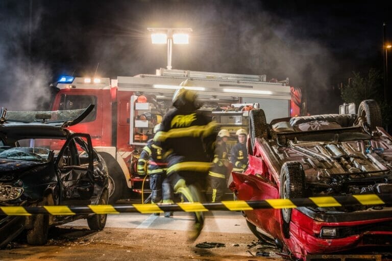 Night shot of a firefighters working on serious traffic accident scene with upside down car, fire engine in background.