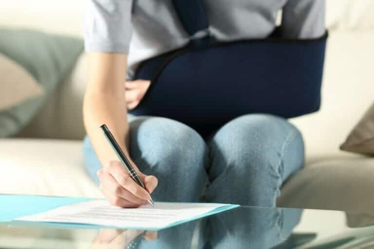 Woman with left arm in a black sling signs workers' compensation forms to begin the claims process.