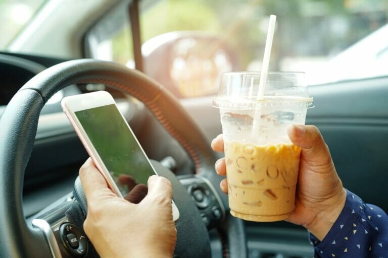 Driver holding ice coffee and mobile phone at car. Concept of distracted driving.