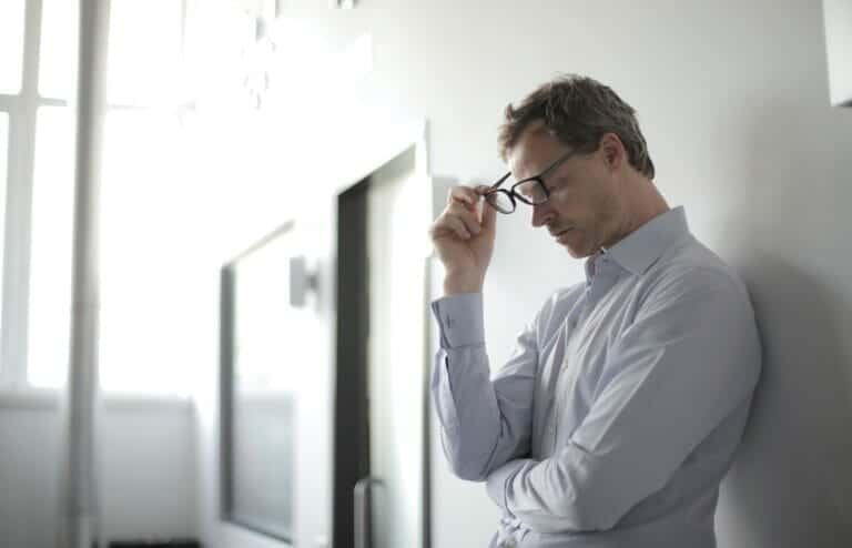 A man propped up against a wall in his home, visibly upset over his recent reputational damage.