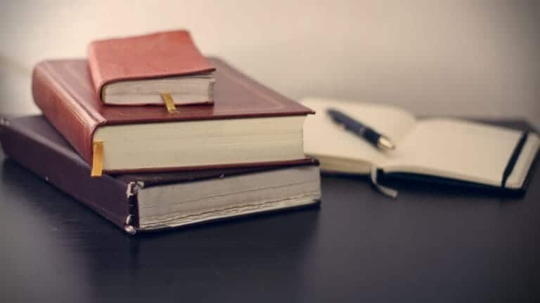 3 brown stacked law books and an open notebook with a pen on it on a black table top