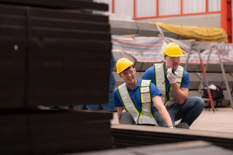 Warehouse employee sitting on the floor with a feelow employee radioing for help because he is injured in an accident where iron fell on his leg