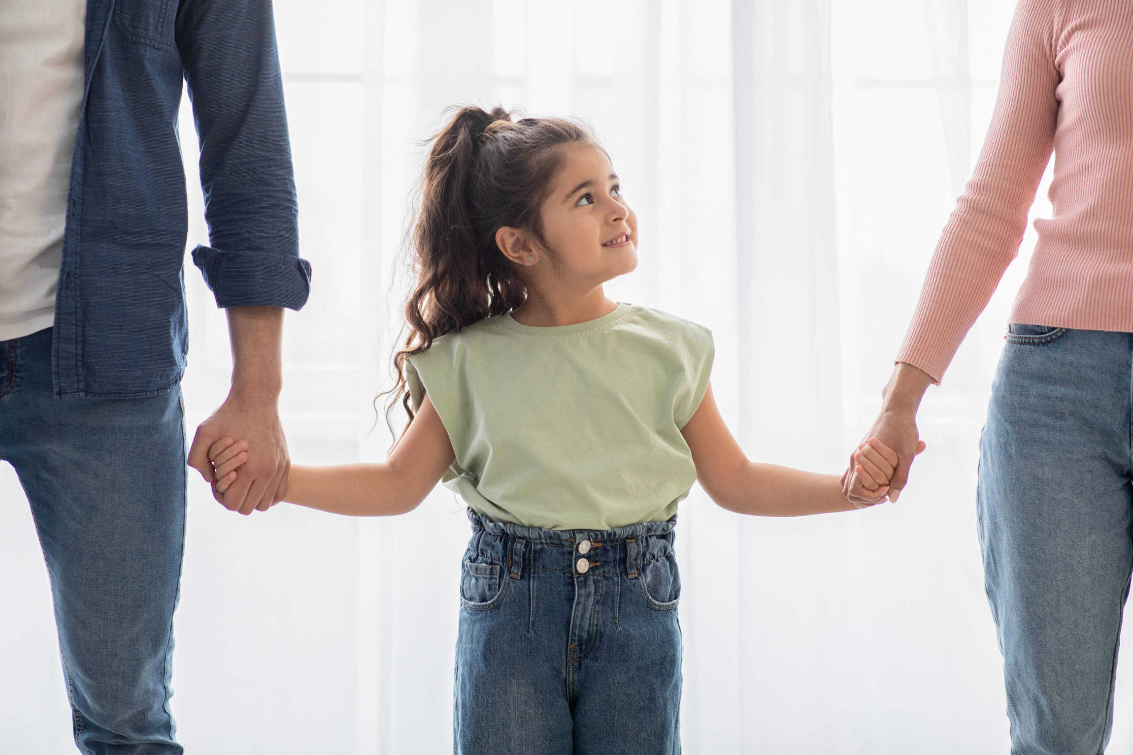 A Child holding onto both of her parents hands.