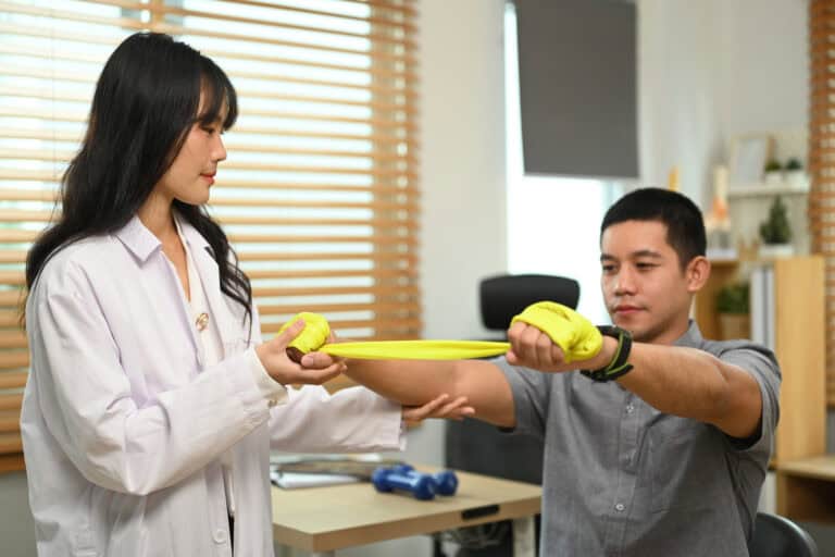 Rehabilitation specialist assisting male patient stretching elastic band during therapy session.