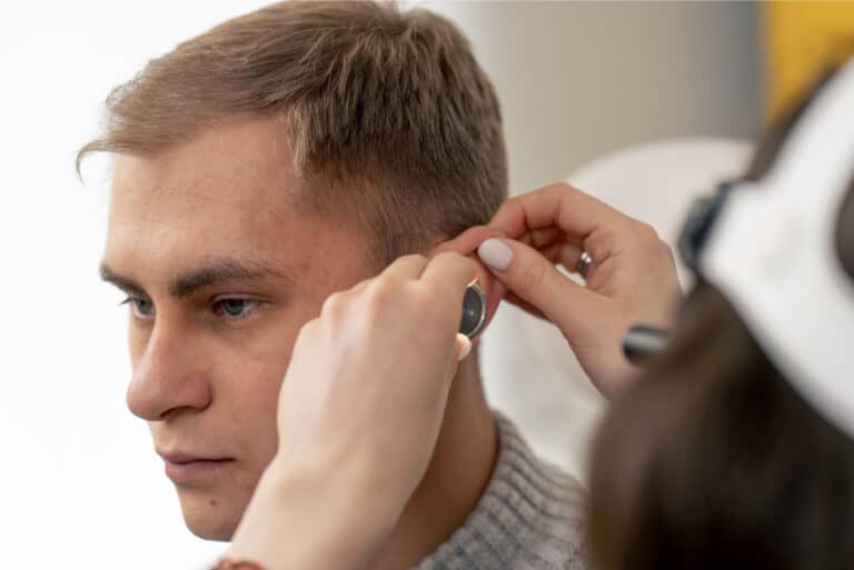 An audiologist examines a man’s ear during a hearing test, checking for signs of work-related hearing loss.