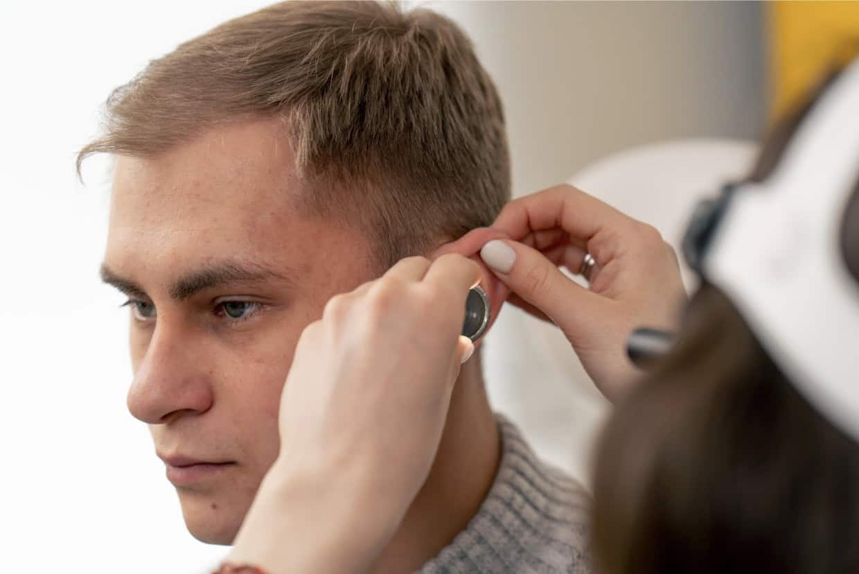 An audiologist examines a man’s ear during a hearing test, checking for signs of work-related hearing loss.