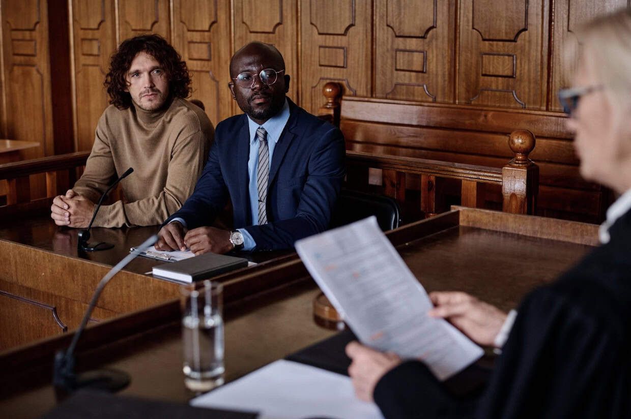 Lawyer and defendant listening to female judge speak with a paper in her hand.