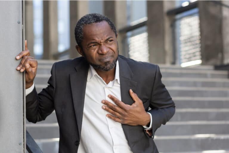 African American man wearing a suit with a hand over his heart, wincing in pain