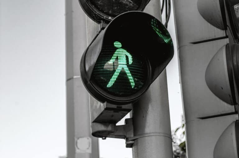 Green pedestrian walk signal illuminated on a crosswalk traffic light mounted to a metal pole at an urban intersection.