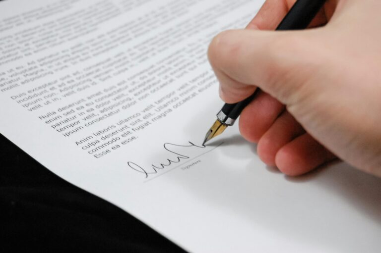 Close-up of a person signing a legal document with a fountain pen, symbolizing the formal execution of a prenuptial agreement.