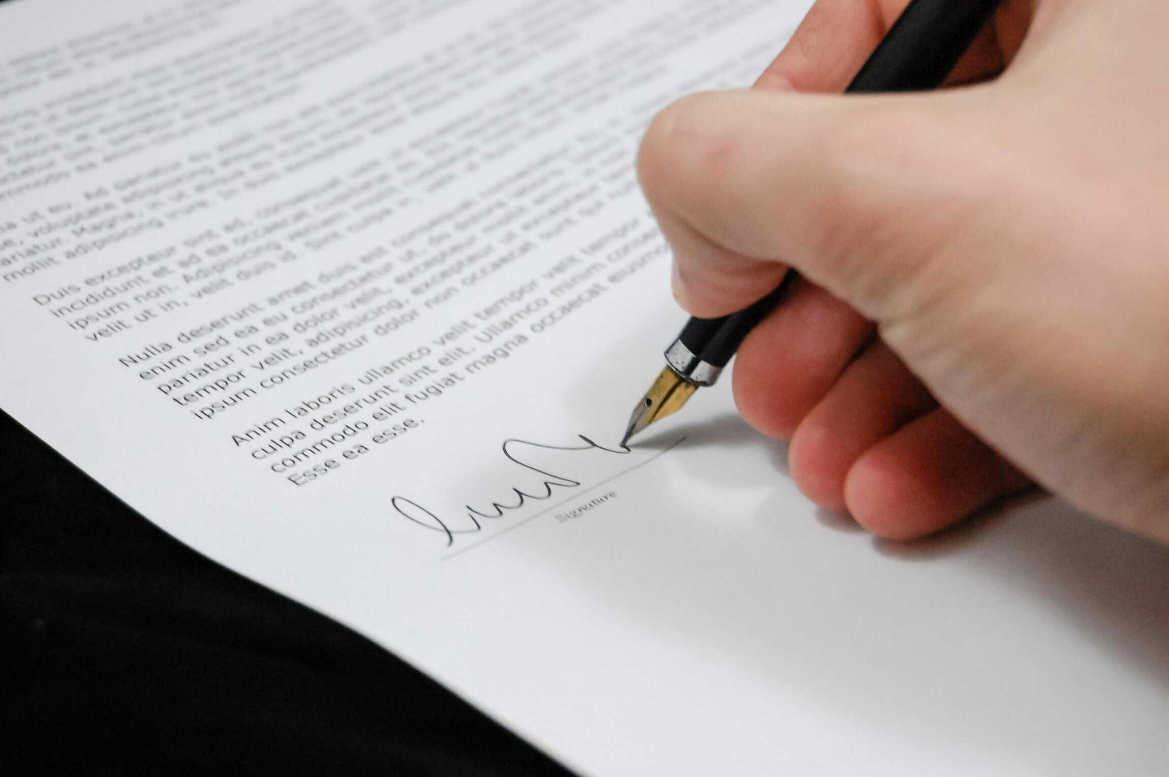 Close-up of a person signing a legal document with a fountain pen, symbolizing the formal execution of a prenuptial agreement.